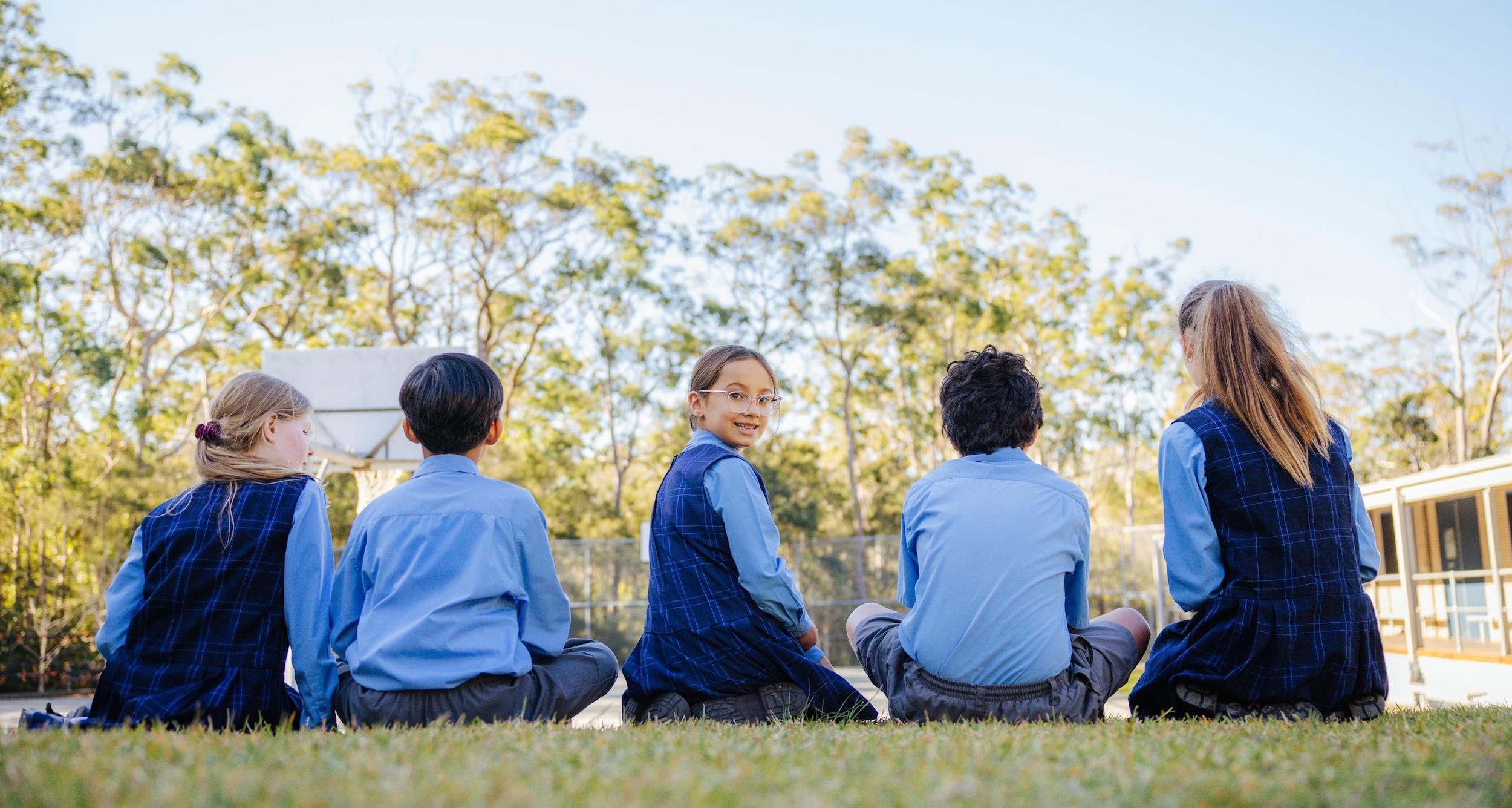 Primary school students seated outdoors on the grass, enjoying a group discussion under clear skies at Medowie Christian School.