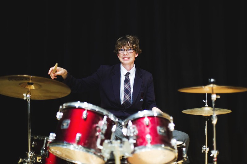 male student in blazer and tie smiling playing drums