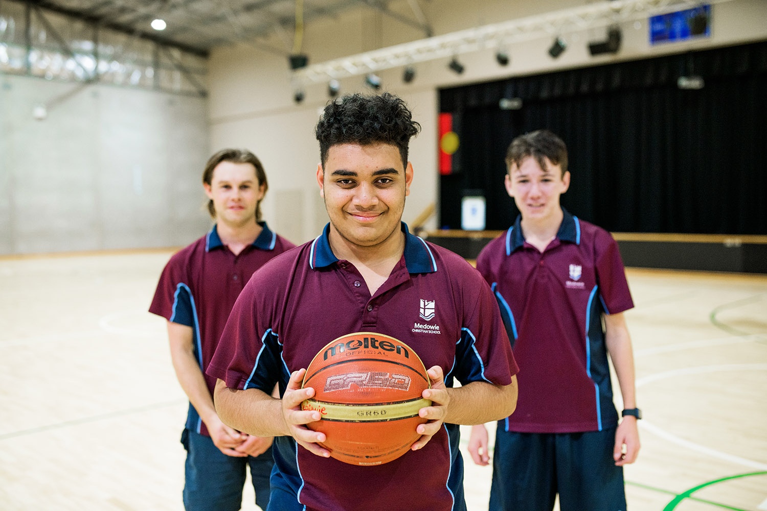 Three male students in sports uniform on Medowie Christian School basketball court
