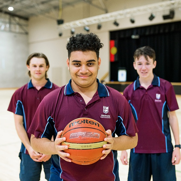 three male students in sports uniform with a basketball