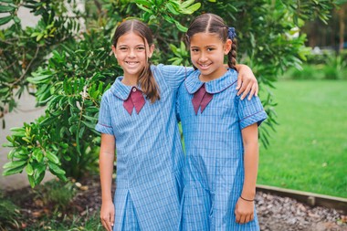 two primary school students in formal uniform with arms around each other smiling